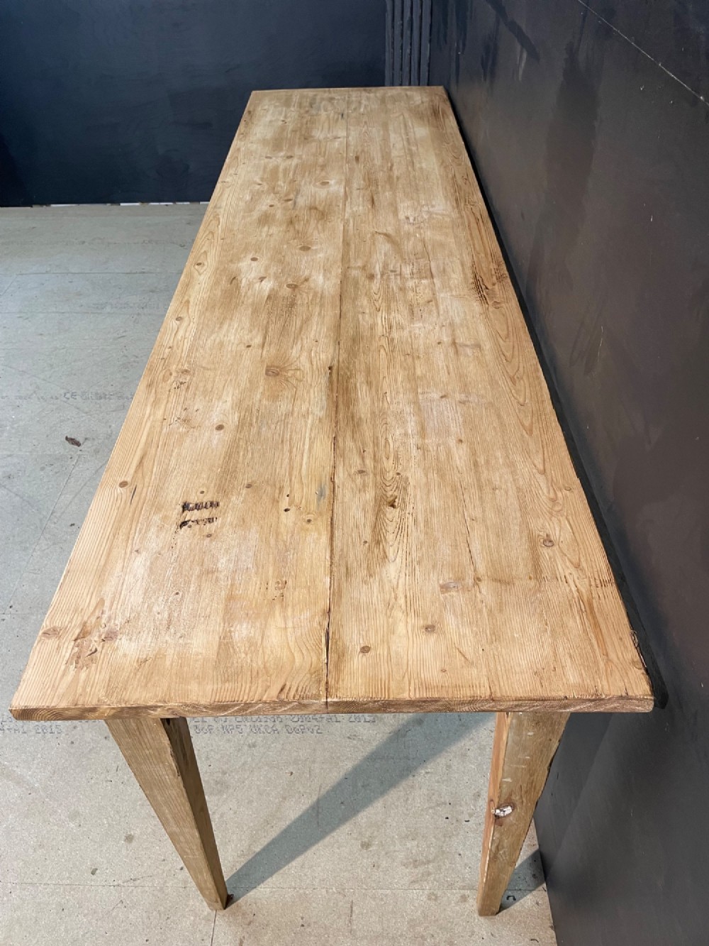 A long scrubbed pine dining table featuring a planked top surface and four tapered square legs. View IV