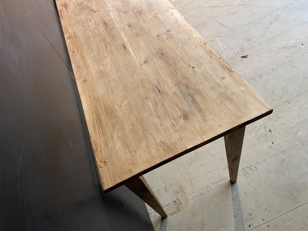 A long scrubbed pine dining table featuring a planked top surface and four tapered square legs. View VII