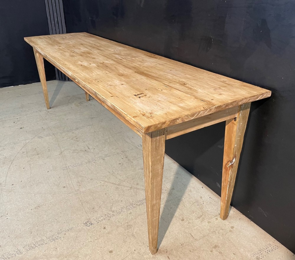 A long scrubbed pine dining table featuring a planked top surface and four tapered square legs.