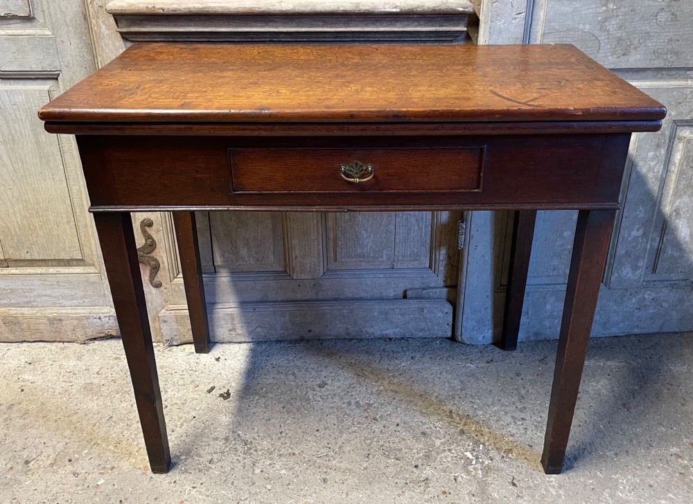 A Georgian oak fold-over tea table featuring a single central frieze drawer with a brass drop handle and straight tapered legs.