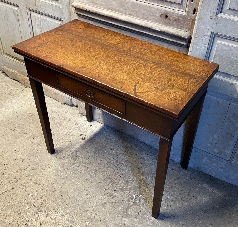 A Georgian oak fold-over tea table featuring a single central frieze drawer with a brass drop handle and straight tapered legs. View IV