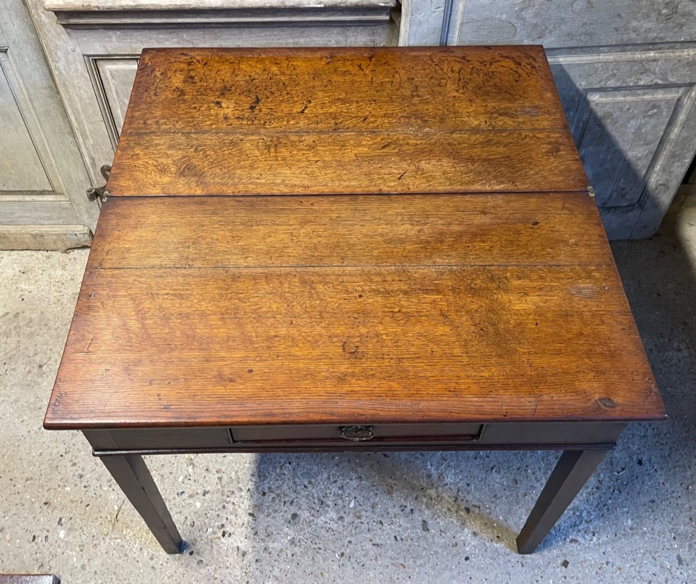 A Georgian oak fold-over tea table featuring a single central frieze drawer with a brass drop handle and straight tapered legs. View V
