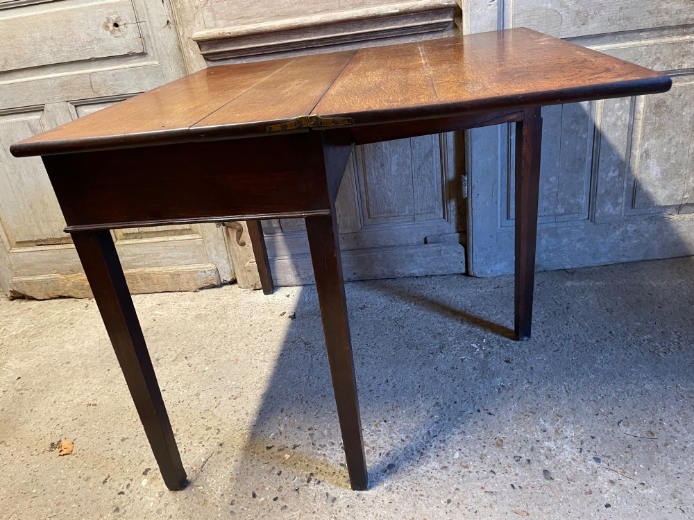 A Georgian oak fold-over tea table featuring a single central frieze drawer with a brass drop handle and straight tapered legs. View VI