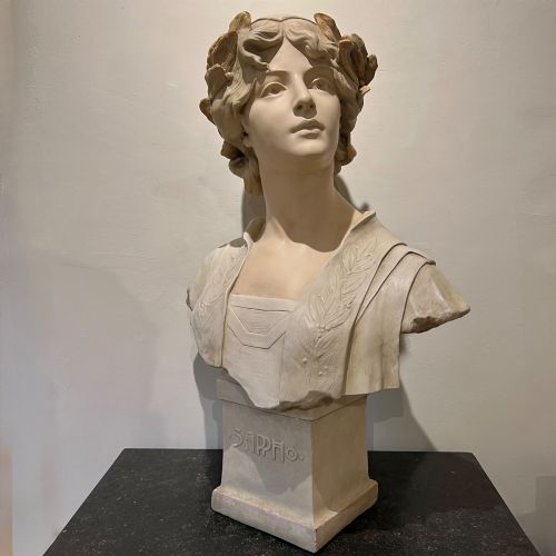 fig 1. An Art Nouveau cream-toned sculptural bust of the classical poet Sappho wearing a golden laurel wreath, mounted on a plinth inscribed with her name.