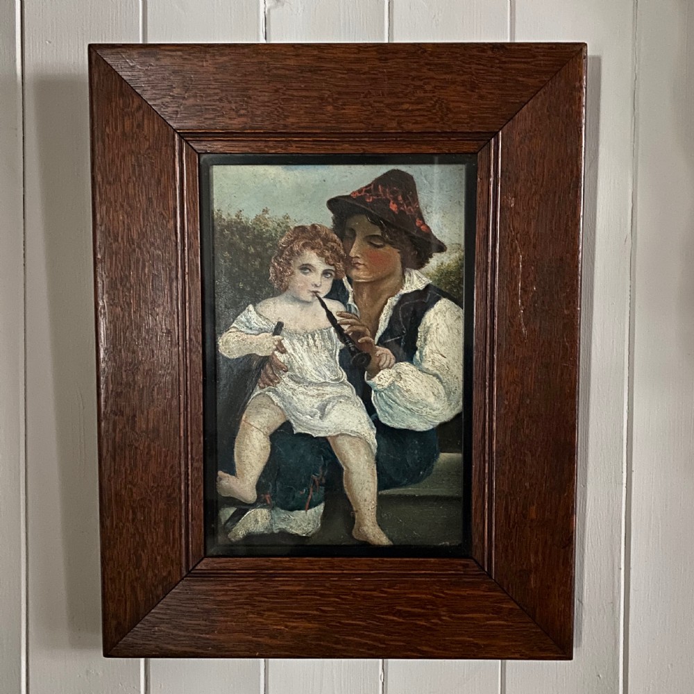 A 19th-century Continental oil painting featuring a seated man holding a young child playing a musical pipe, enclosed within a wide dark oak moulded frame.