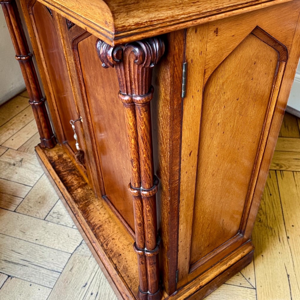 A William IV Gothic Revival oak side cabinet featuring twin pointed-arch panelled doors flanked by turned columns. View IV