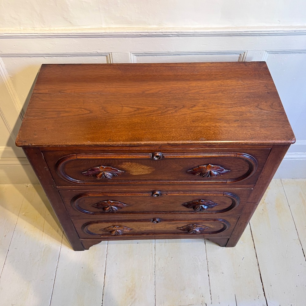 A late nineteenth-century American oak chest featuring three drawers with oval moulding and carved wooden foliate handles. View V
