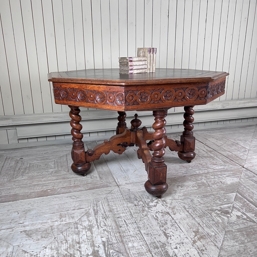 An octagonal Victorian oak centre table featuring a carved rosette frieze, barley twist legs, a central finial stretcher, and an inset leather top.