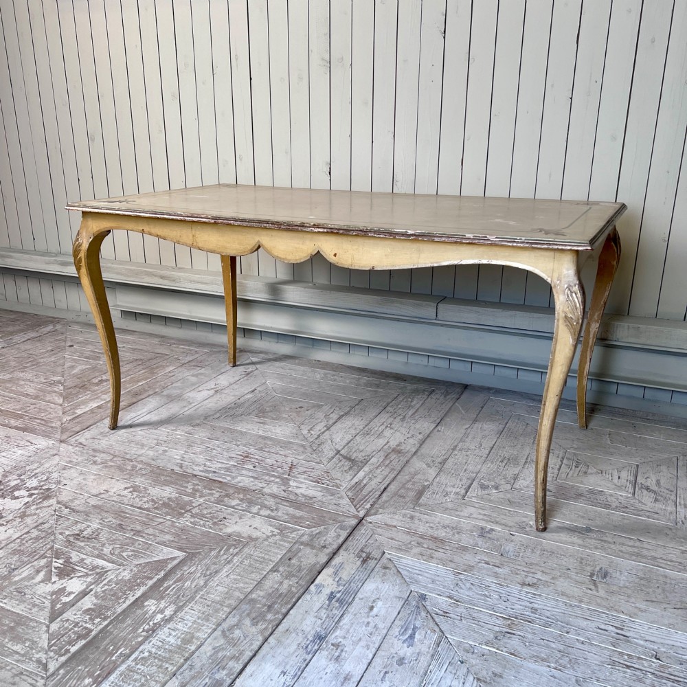 A rectangular French Louis XV Revival dining table featuring a cream painted finish, gold leaf accents, curved cabriole legs, and a scalloped apron. View III