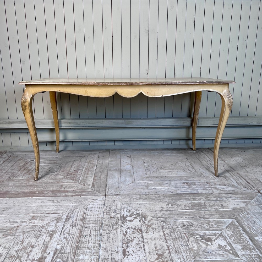 A rectangular French Louis XV Revival dining table featuring a cream painted finish, gold leaf accents, curved cabriole legs, and a scalloped apron. View X