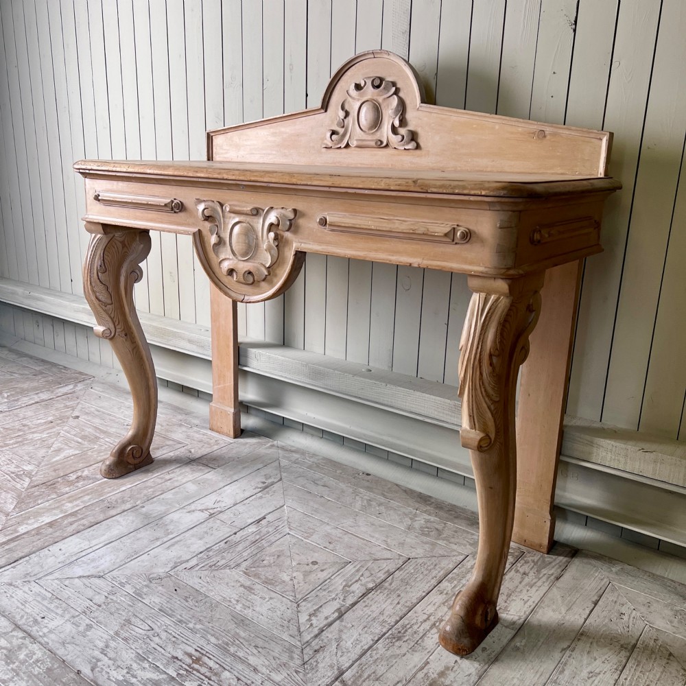 A Victorian carved pine console table featuring front cabriole legs, a central relief cartouche, and a shaped gallery backrest.