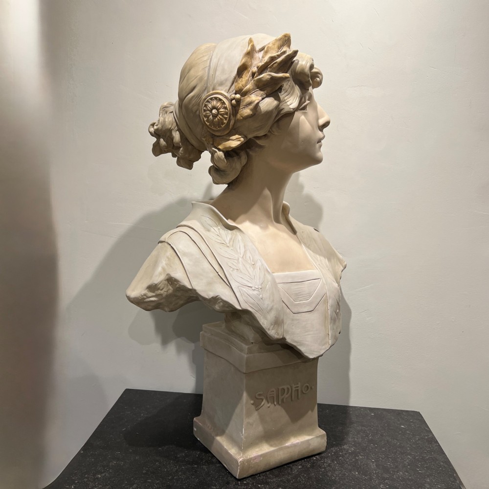 An Art Nouveau cream-toned sculptural bust of the classical poet Sappho wearing a golden laurel wreath, mounted on a plinth inscribed with her name. View III