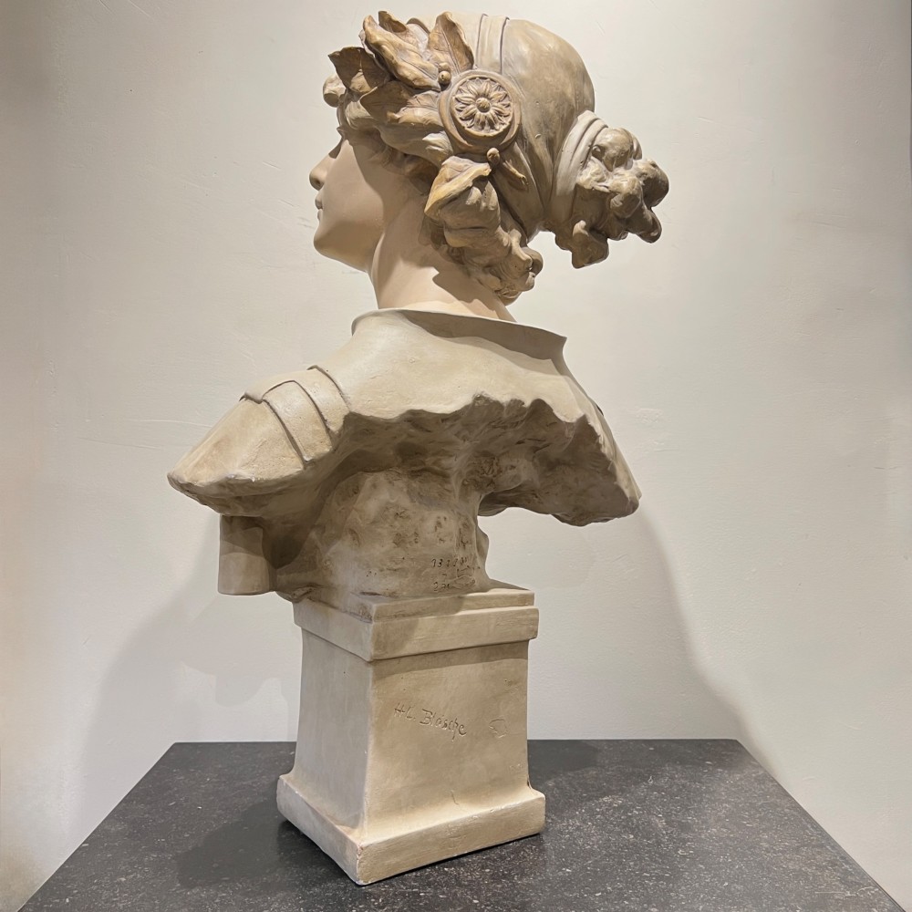An Art Nouveau cream-toned sculptural bust of the classical poet Sappho wearing a golden laurel wreath, mounted on a plinth inscribed with her name. View IV