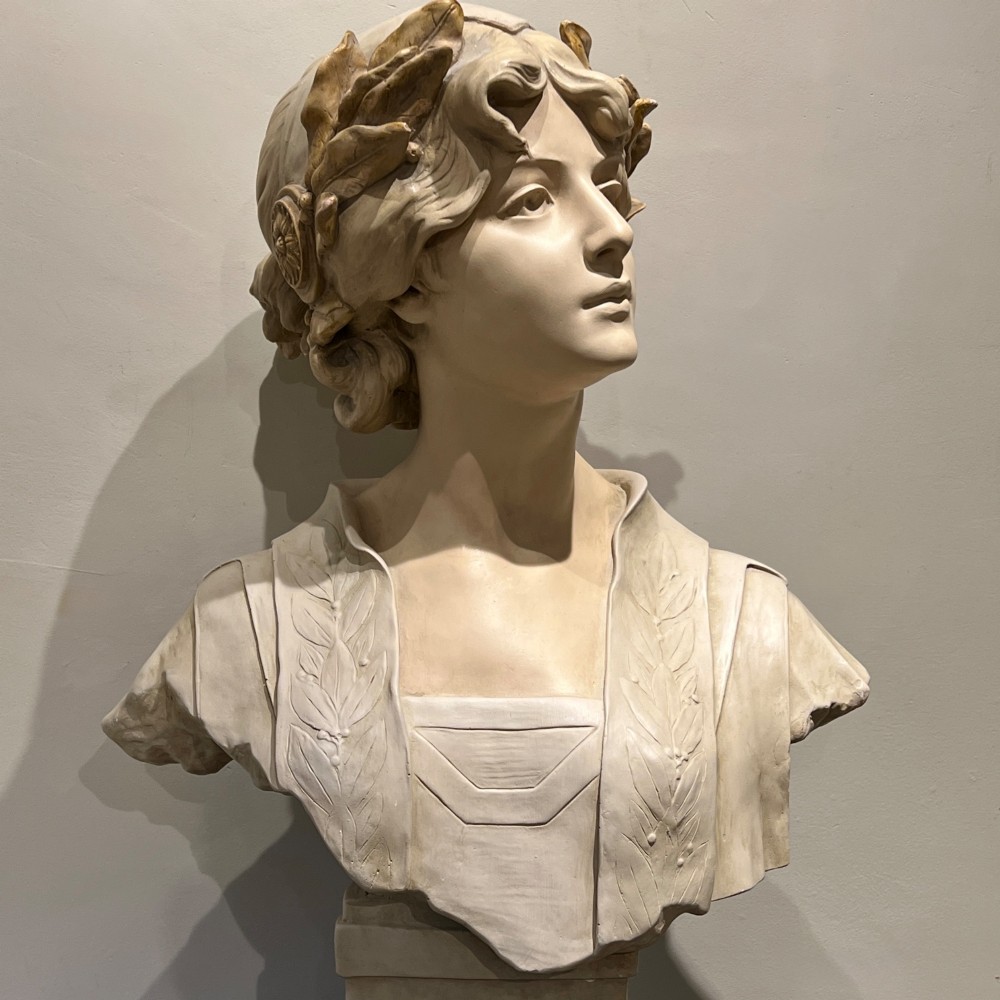 An Art Nouveau cream-toned sculptural bust of the classical poet Sappho wearing a golden laurel wreath, mounted on a plinth inscribed with her name. View V