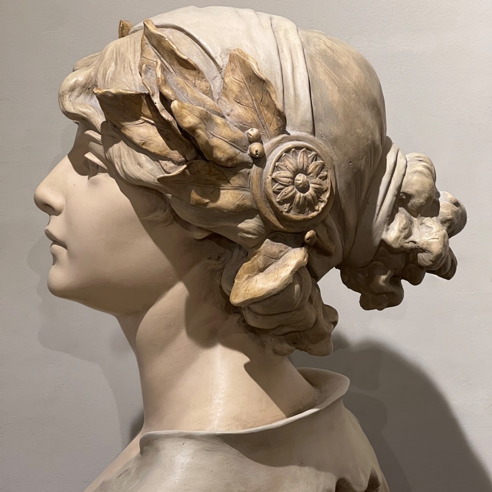 An Art Nouveau cream-toned sculptural bust of the classical poet Sappho wearing a golden laurel wreath, mounted on a plinth inscribed with her name. View VIII