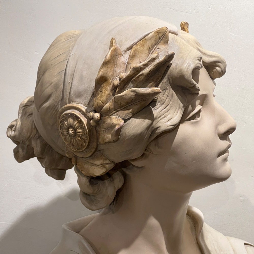 An Art Nouveau cream-toned sculptural bust of the classical poet Sappho wearing a golden laurel wreath, mounted on a plinth inscribed with her name. View IX