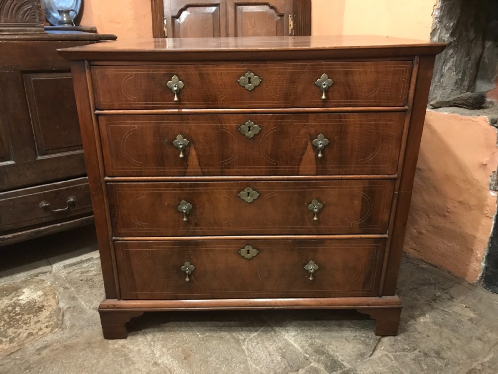 An early eighteenth-century walnut chest of drawers featuring four graduated drawers with geometric stringing inlay, brass teardrop handles, and bracket feet.