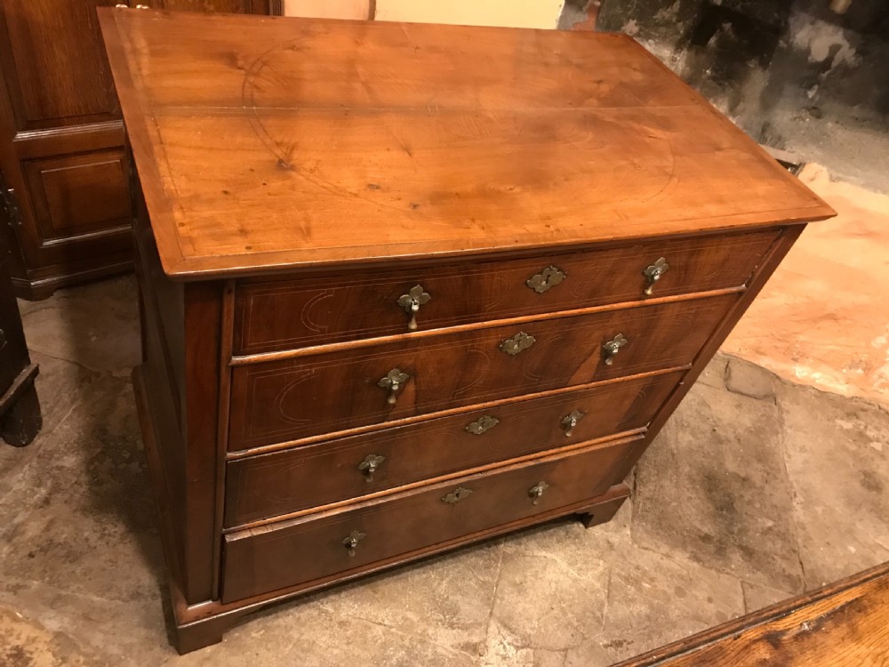 An early eighteenth-century walnut chest of drawers featuring four graduated drawers with geometric stringing inlay, brass teardrop handles, and bracket feet. View II