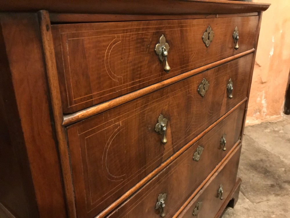 An early eighteenth-century walnut chest of drawers featuring four graduated drawers with geometric stringing inlay, brass teardrop handles, and bracket feet. View IV