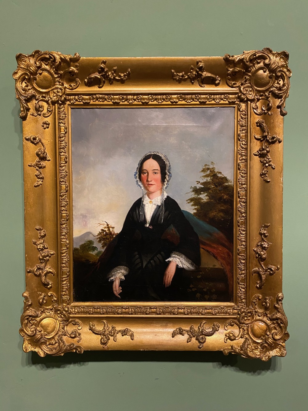 A 19th-century oil portrait depicting a seated lady in formal lace bonnet and black dress inside an ornate giltwood frame.