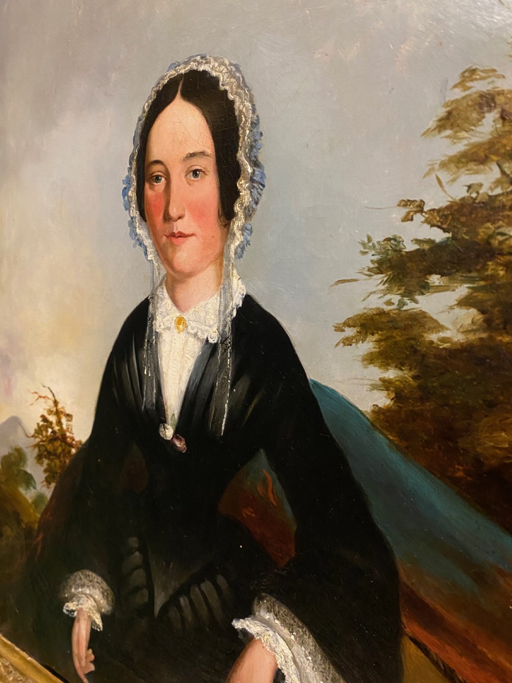 A 19th-century oil portrait depicting a seated lady in formal lace bonnet and black dress inside an ornate giltwood frame. View II