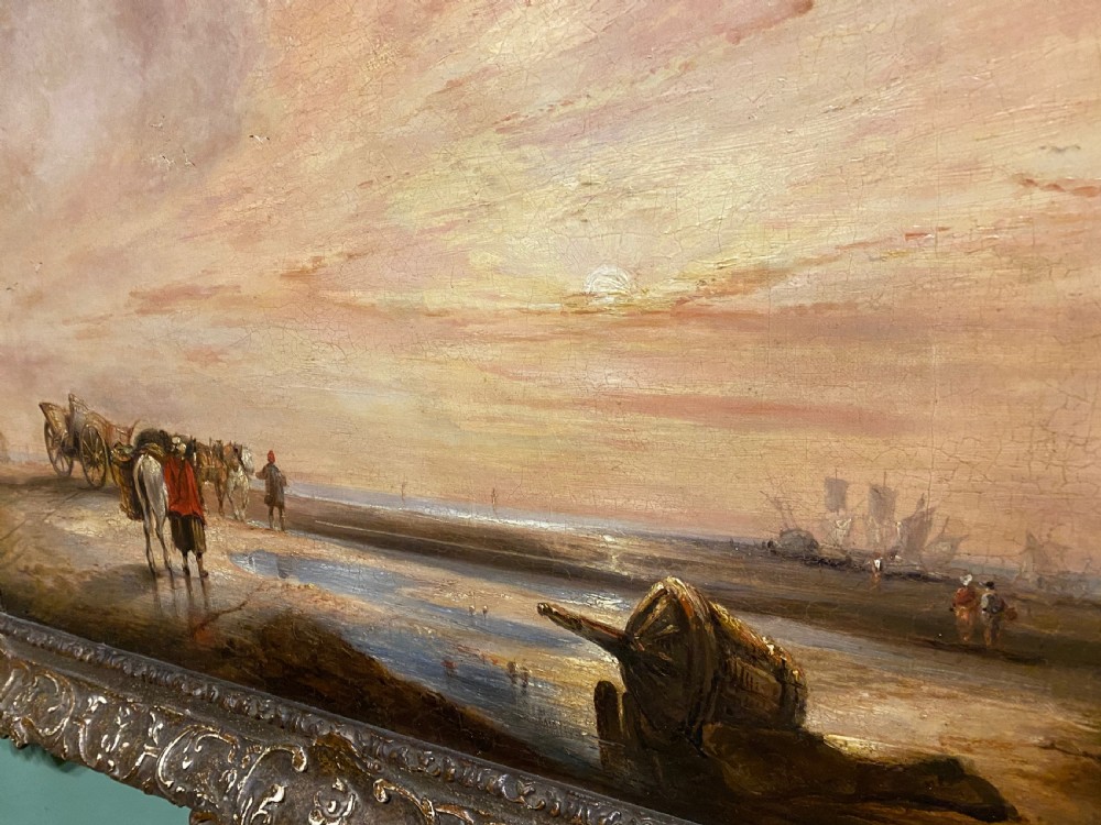 A nineteenth-century coastal oil painting depicting figures and horse-drawn carts on a shore at low tide during sunset, framed in an ornate gilded frame. View II