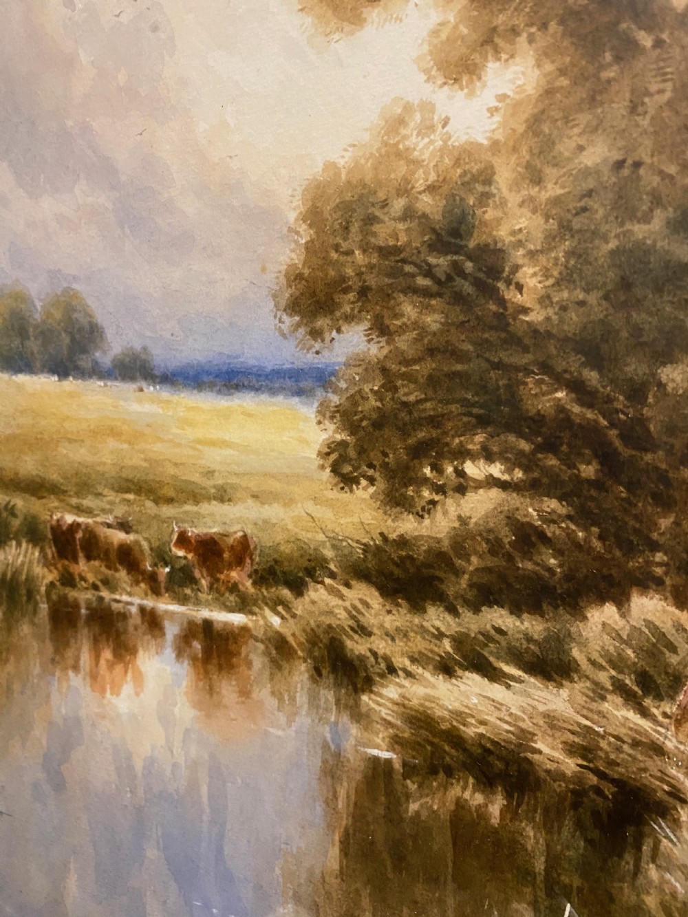 A 19th-century framed watercolour landscape painting depicting cattle resting by a river bank alongside trees, enclosed within a gold swept frame. View IV