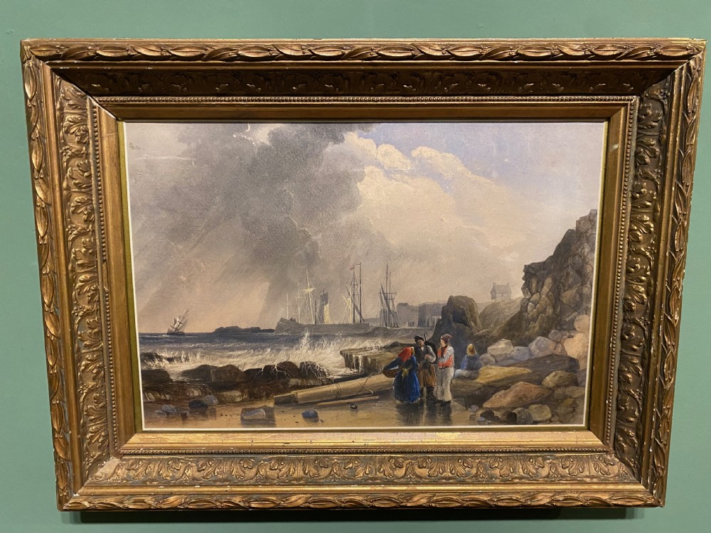 A framed 19th-century watercolour painting depicting fishermen on a rocky shore beside stormy seas, enclosed in an ornate gilded frame.