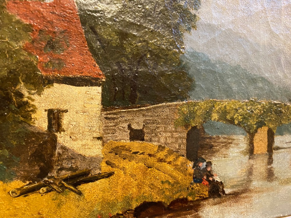 A 19th-century oil painting on canvas depicting a rural river scene with a stone bridge, village cottages, and seated figures on a grassy bank, presented in a dark wooden frame with gilt trim. View II