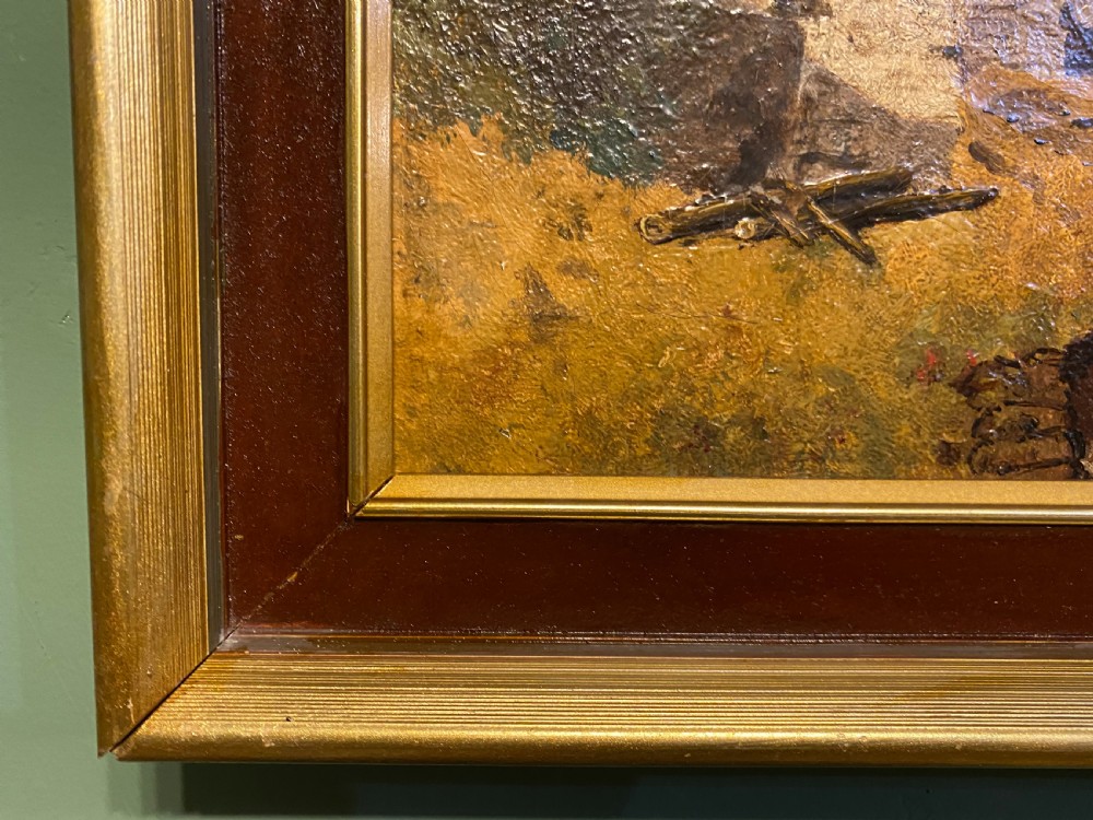 A 19th-century oil painting on canvas depicting a rural river scene with a stone bridge, village cottages, and seated figures on a grassy bank, presented in a dark wooden frame with gilt trim. View III