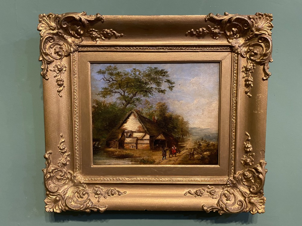 A 19th-century oil painting on canvas depicting a rural thatched farmhouse cottage surrounded by trees, displayed inside an ornate gilded frame.