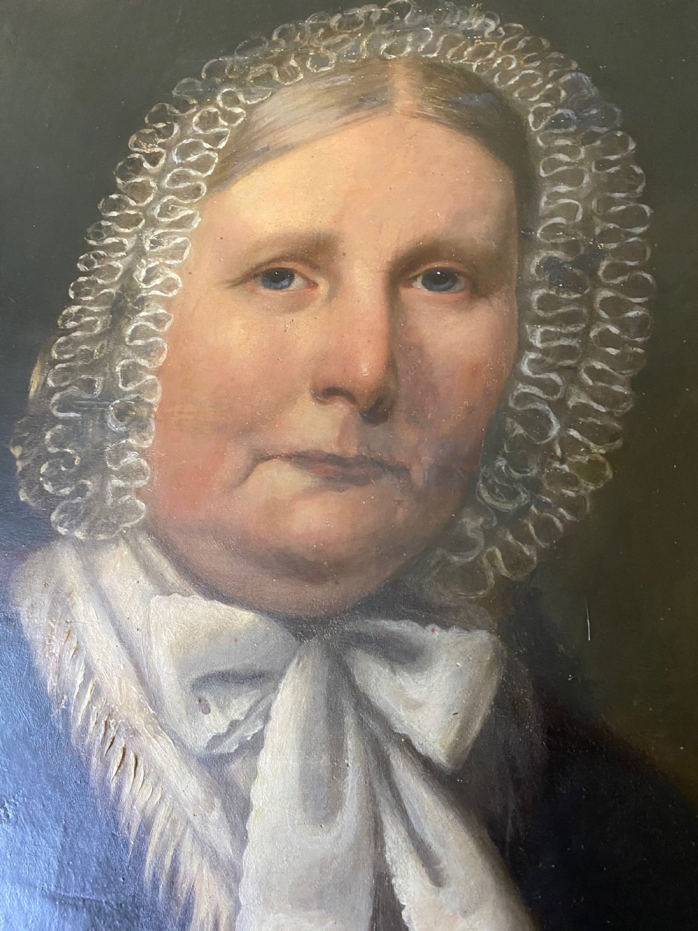 A 19th-century oil portrait depicting a seated woman wearing a lace bonnet and white neckerchief, contained in a black wooden frame with a gold inner slip. View II