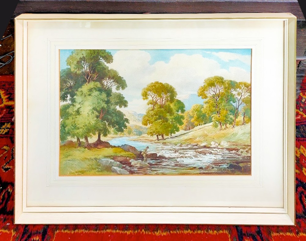 A framed watercolour landscape painting depicting a fisherman standing on rocks in a rushing river surrounded by mature trees.