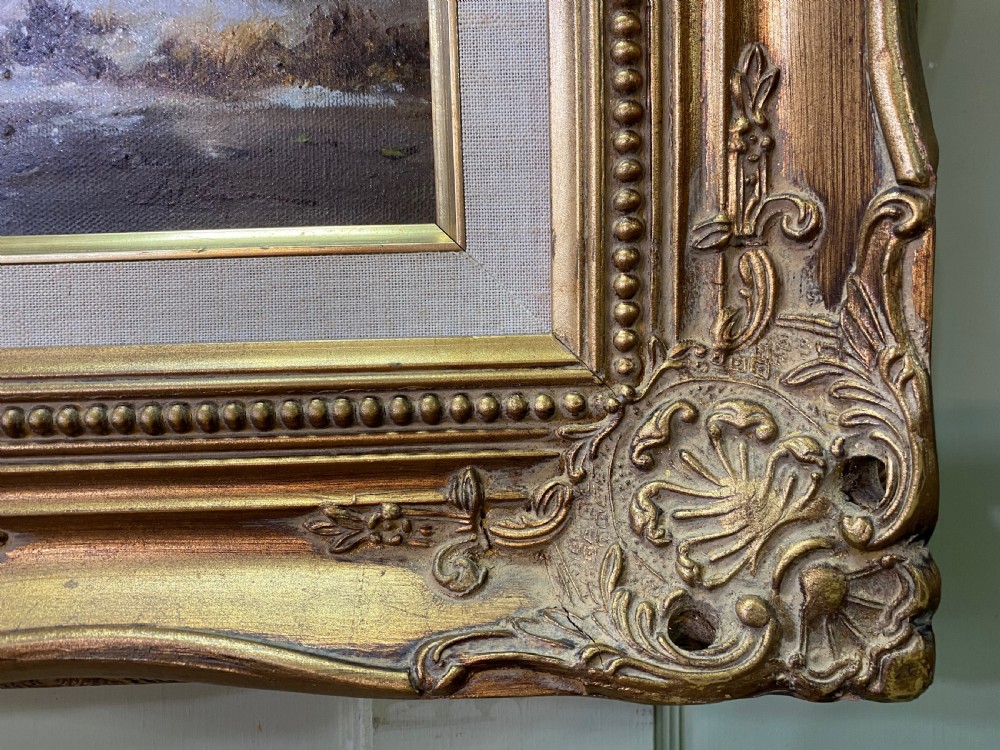 An oil painting depicting a winter landscape with figures near a thatched cottage on a frozen river, set in an ornate giltwood frame. View IV