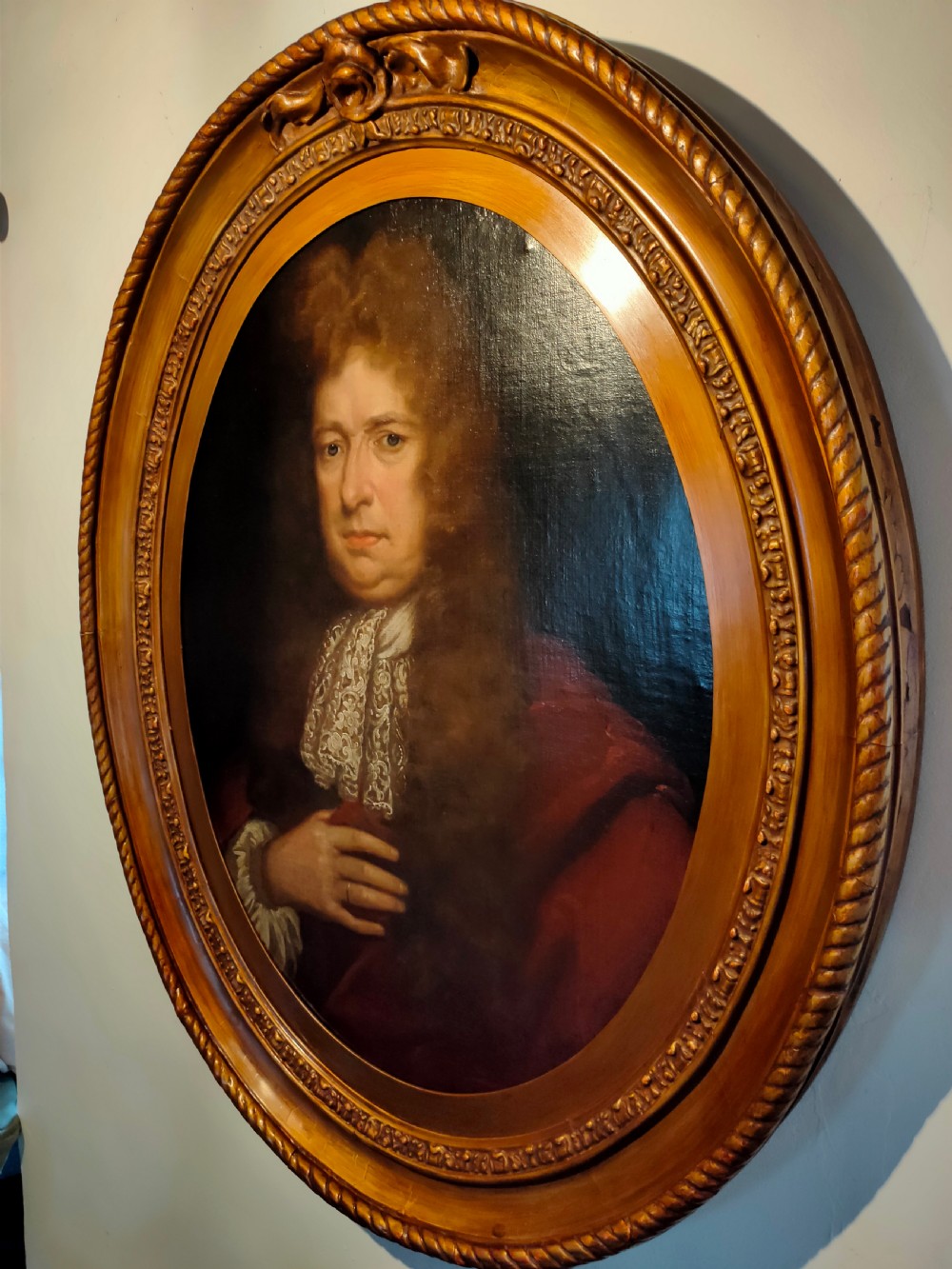 A seventeenth-century oval oil painting on canvas depicting a gentleman with a long wig, lace cravat, and crimson cloak, set within a carved wood frame. View III