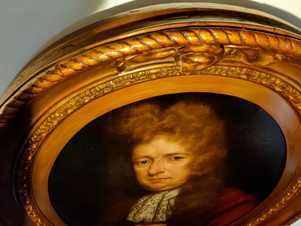 A seventeenth-century oval oil painting on canvas depicting a gentleman with a long wig, lace cravat, and crimson cloak, set within a carved wood frame. View V