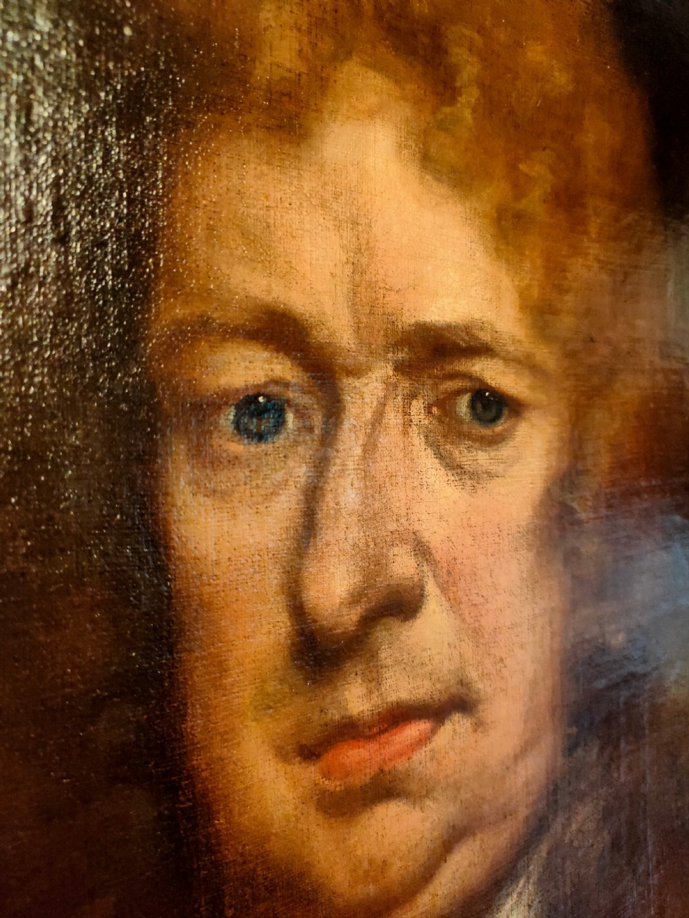 A seventeenth-century oval oil painting on canvas depicting a gentleman with a long wig, lace cravat, and crimson cloak, set within a carved wood frame. View VI