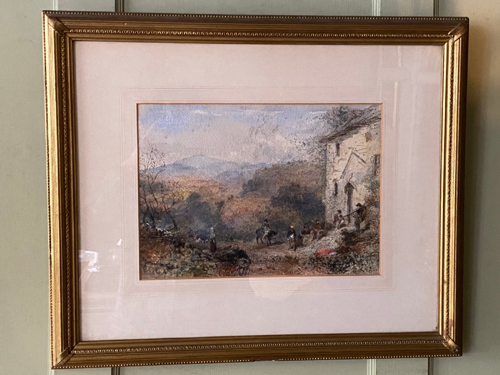 An early 20th-century watercolour painting depicting figures near a rustic stone building in a hilly landscape, presented in a gilded frame.