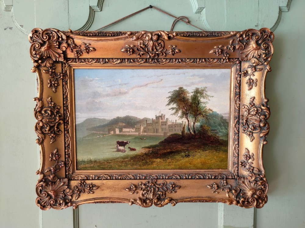 A 19th-century oil painting on canvas depicting Lowther Castle in a green landscape with cattle, encased in an ornate gold frame.