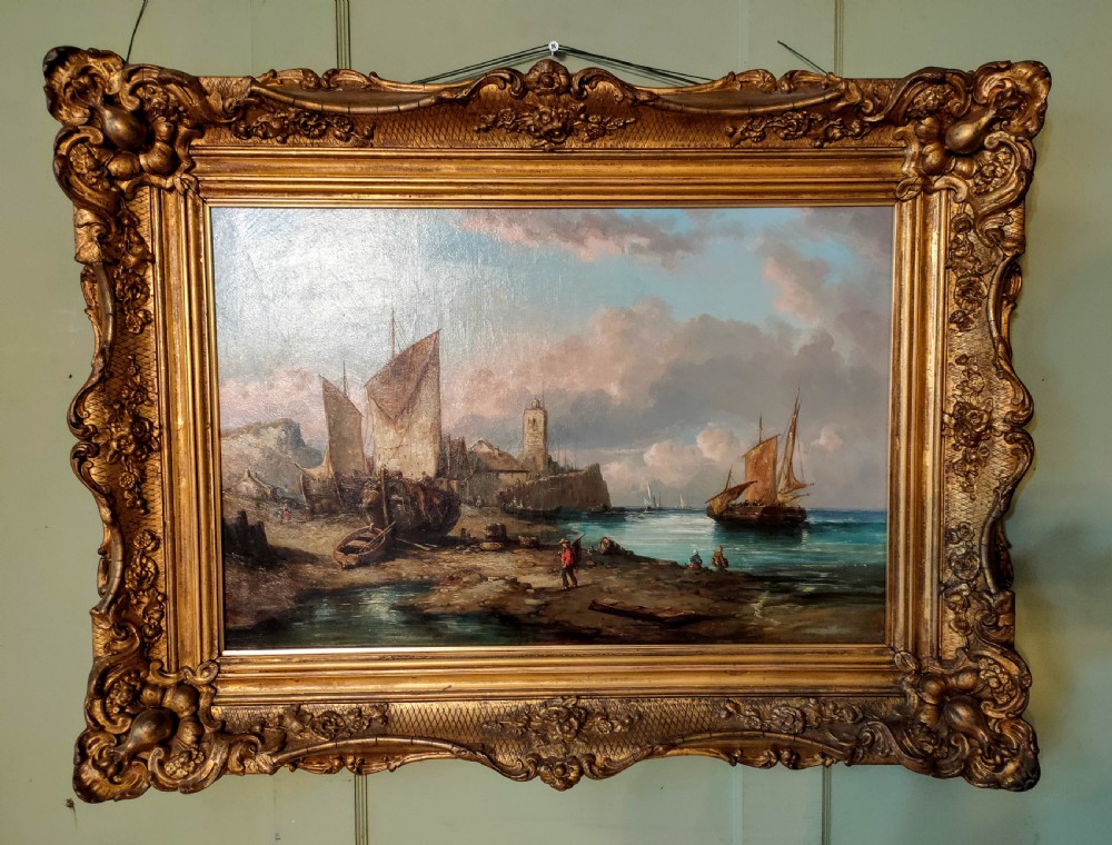 A 19th-century oil painting depicting fishermen and sailing vessels in a coastal harbour, housed in an ornate gilt swept frame.
