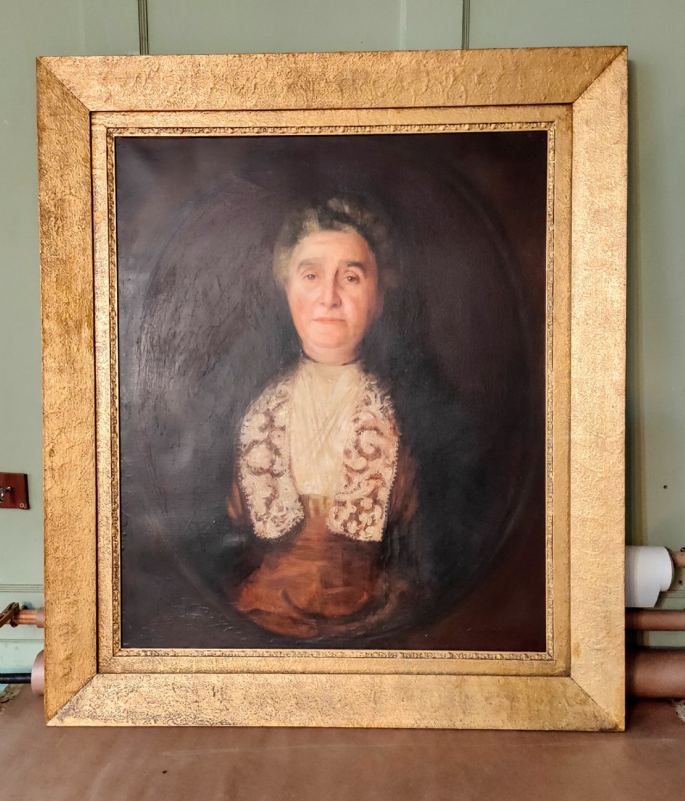 An antique oil painting depicting an elder woman in a lace stole set against a dark background within a wide gilt frame.