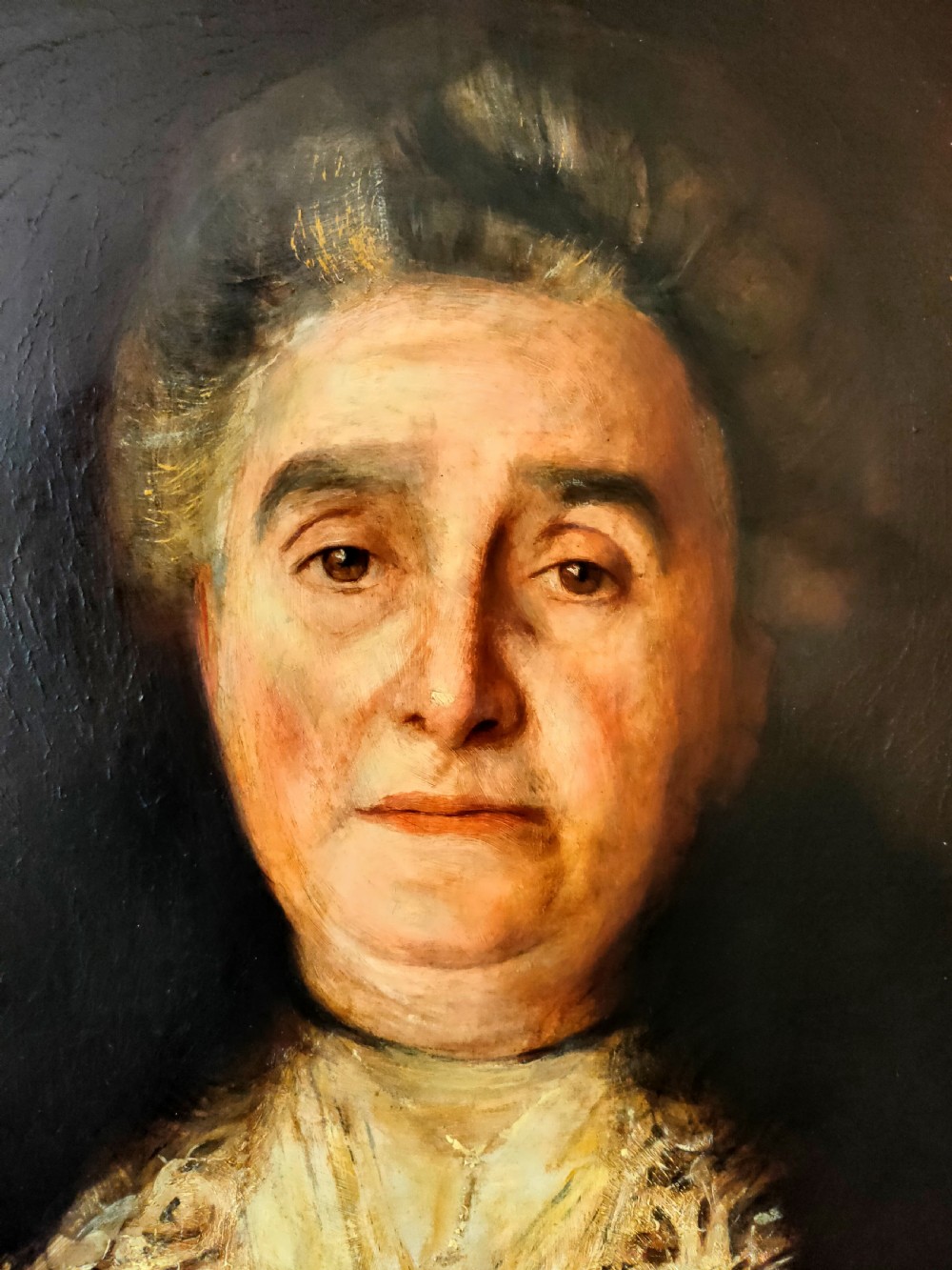 An antique oil painting depicting an elder woman in a lace stole set against a dark background within a wide gilt frame. View III