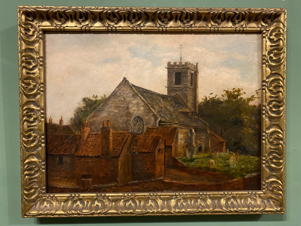 An antique 19th-century oil painting depicting a stone village church and cottages set within an ornate gilded frame.