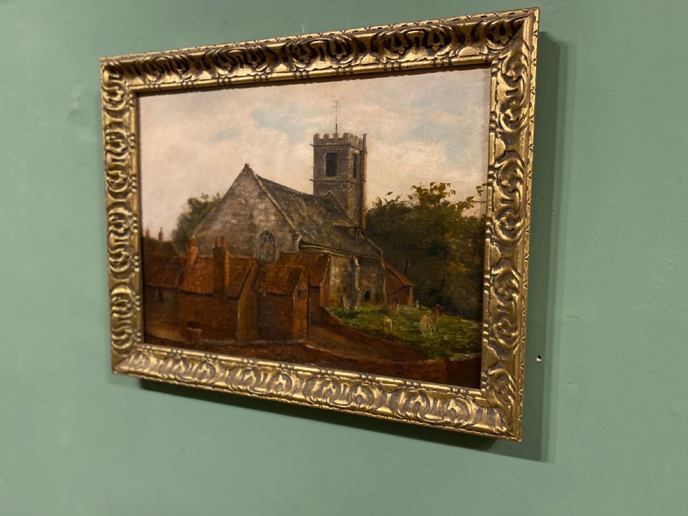 An antique 19th-century oil painting depicting a stone village church and cottages set within an ornate gilded frame. View III