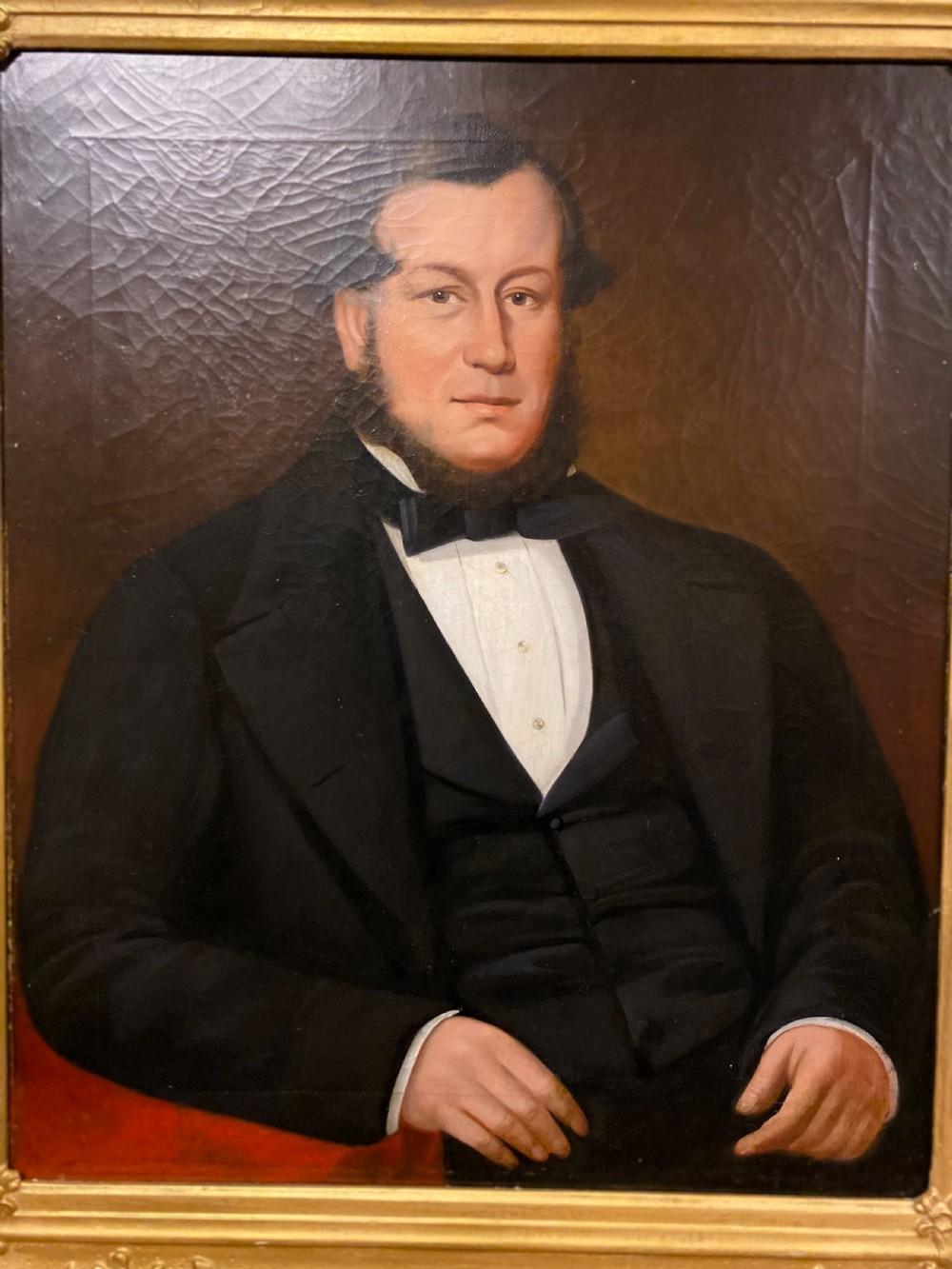 A 19th-century oil painting on canvas depicting a seated gentleman in black formal wear, set within an ornate gilded frame. View III