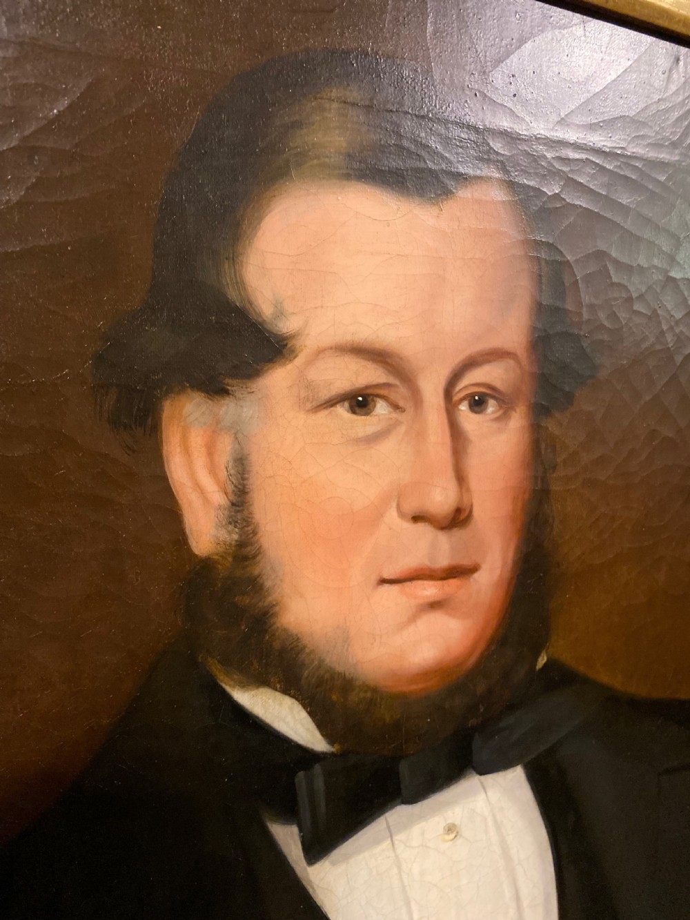 A 19th-century oil painting on canvas depicting a seated gentleman in black formal wear, set within an ornate gilded frame. View IV
