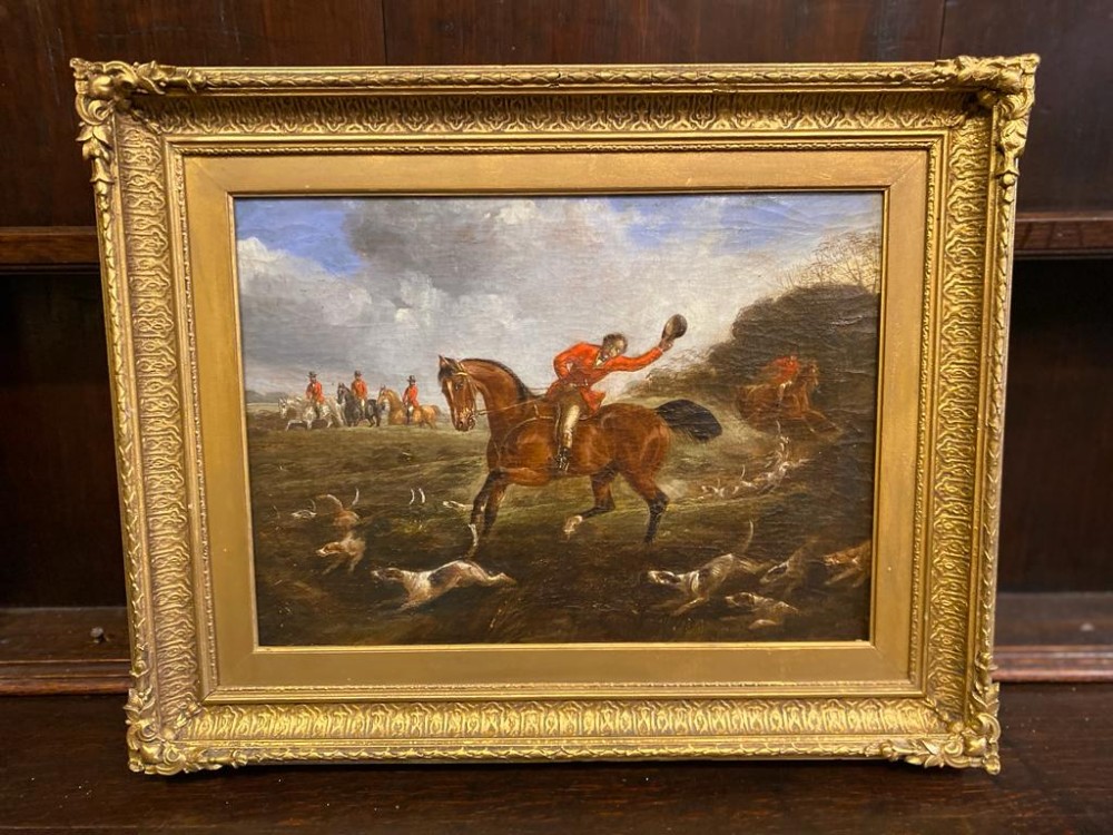 A nineteenth-century oil painting depicting a huntsman in a red coat riding a brown horse alongside hounds, framed in an ornate gold gilt frame.