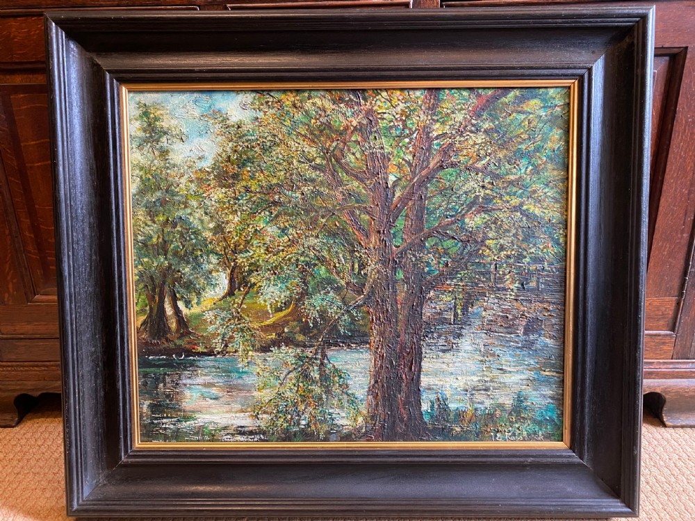 A framed oil painting featuring a heavily textured woodland riverbank scene with large trees leaning over a body of water in a dark wooden frame.