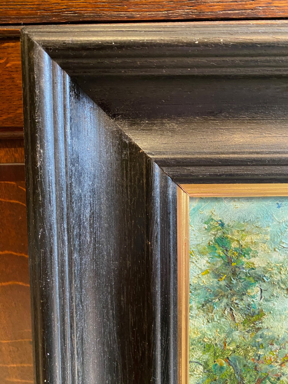 A framed oil painting featuring a heavily textured woodland riverbank scene with large trees leaning over a body of water in a dark wooden frame. View IV