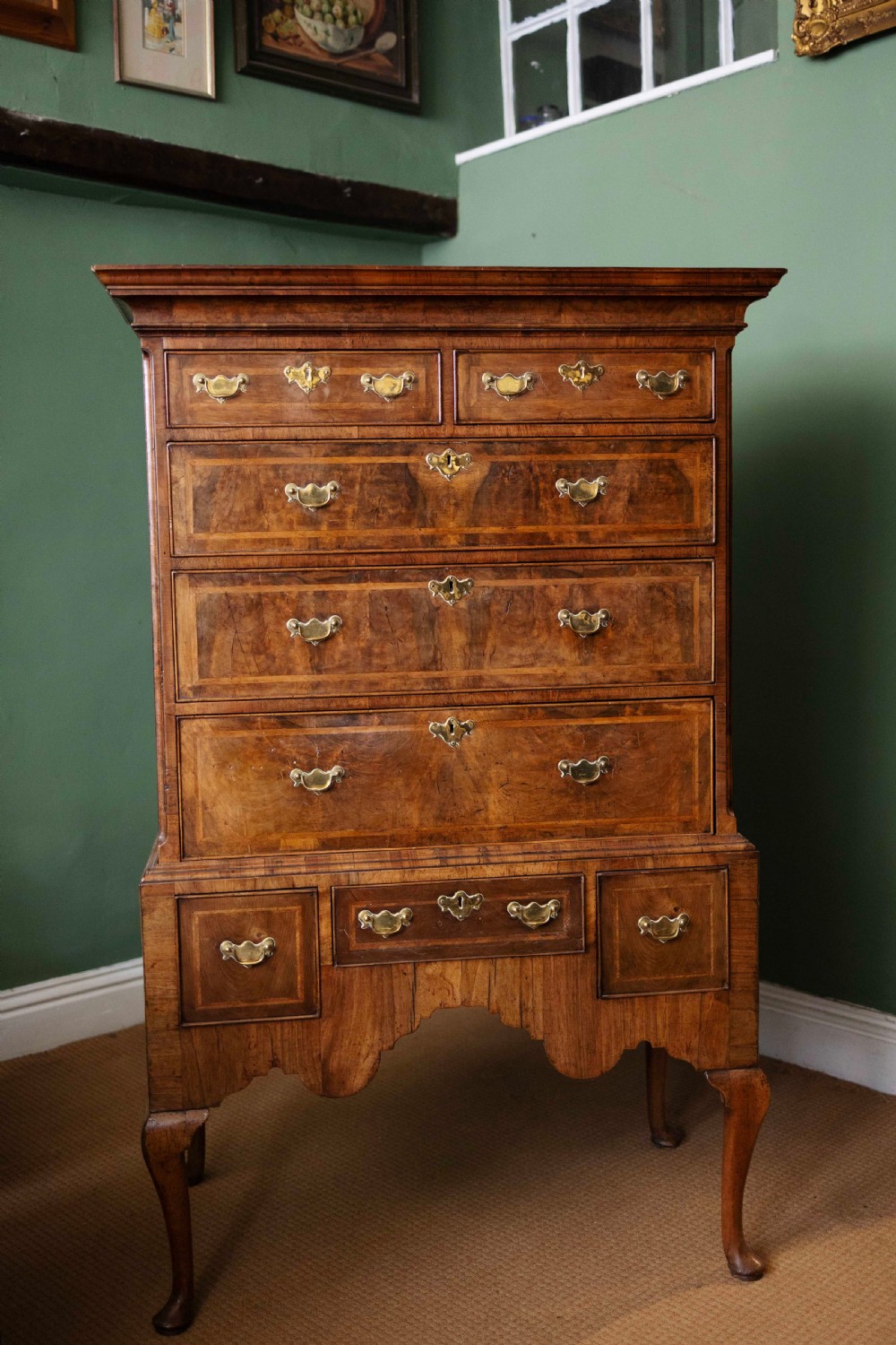 An early 18th-century walnut chest on stand with multiple crossbanded drawers, brass handles, a scalloped apron, and cabriole legs.